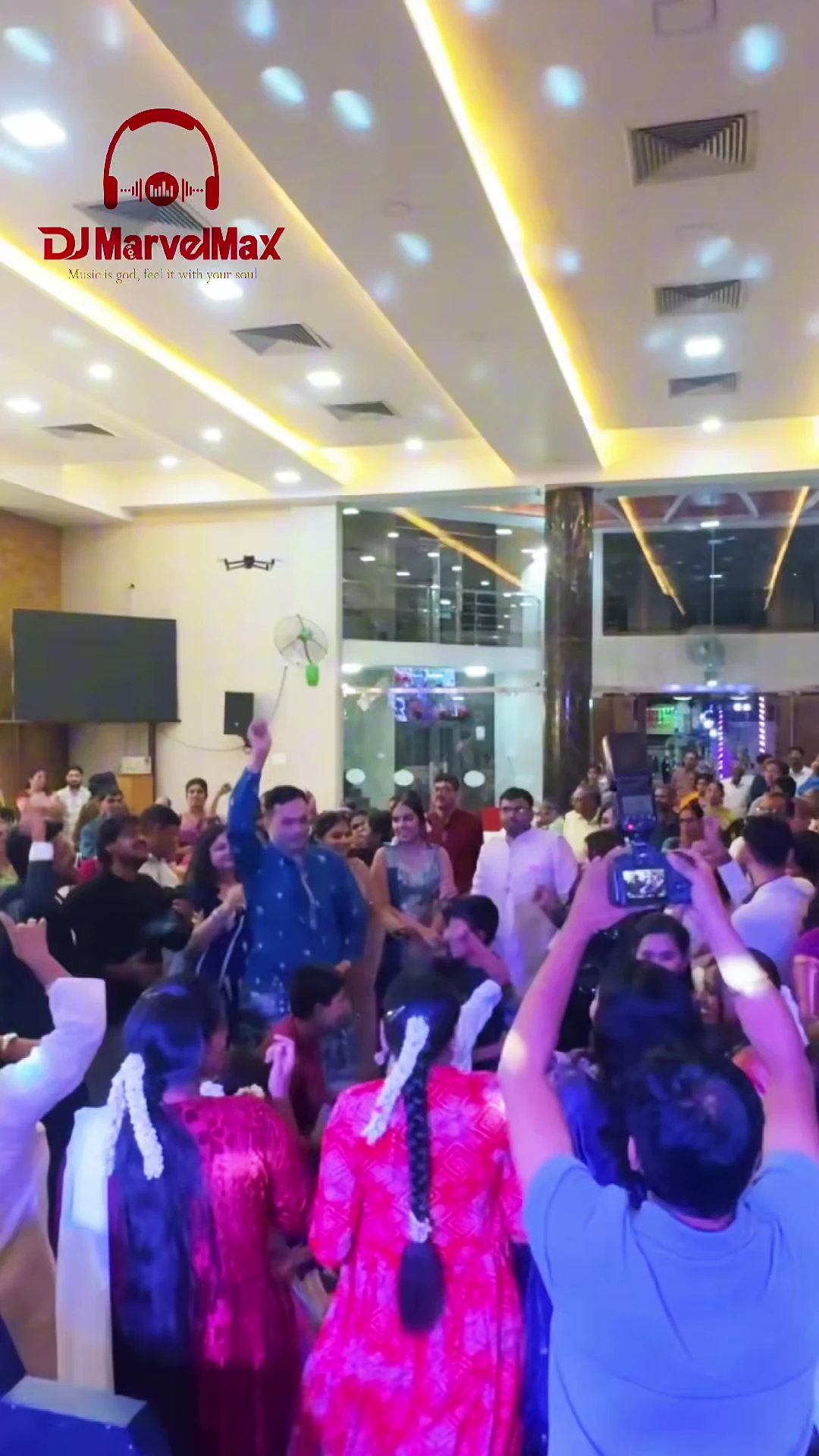 Guests dancing in a bright indoor hall with colourful lighting and the MarvelMax DJ booth