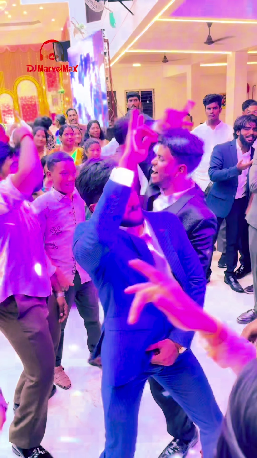 Guests dancing beneath warm reception lights, with a man in a blue suit at the centre