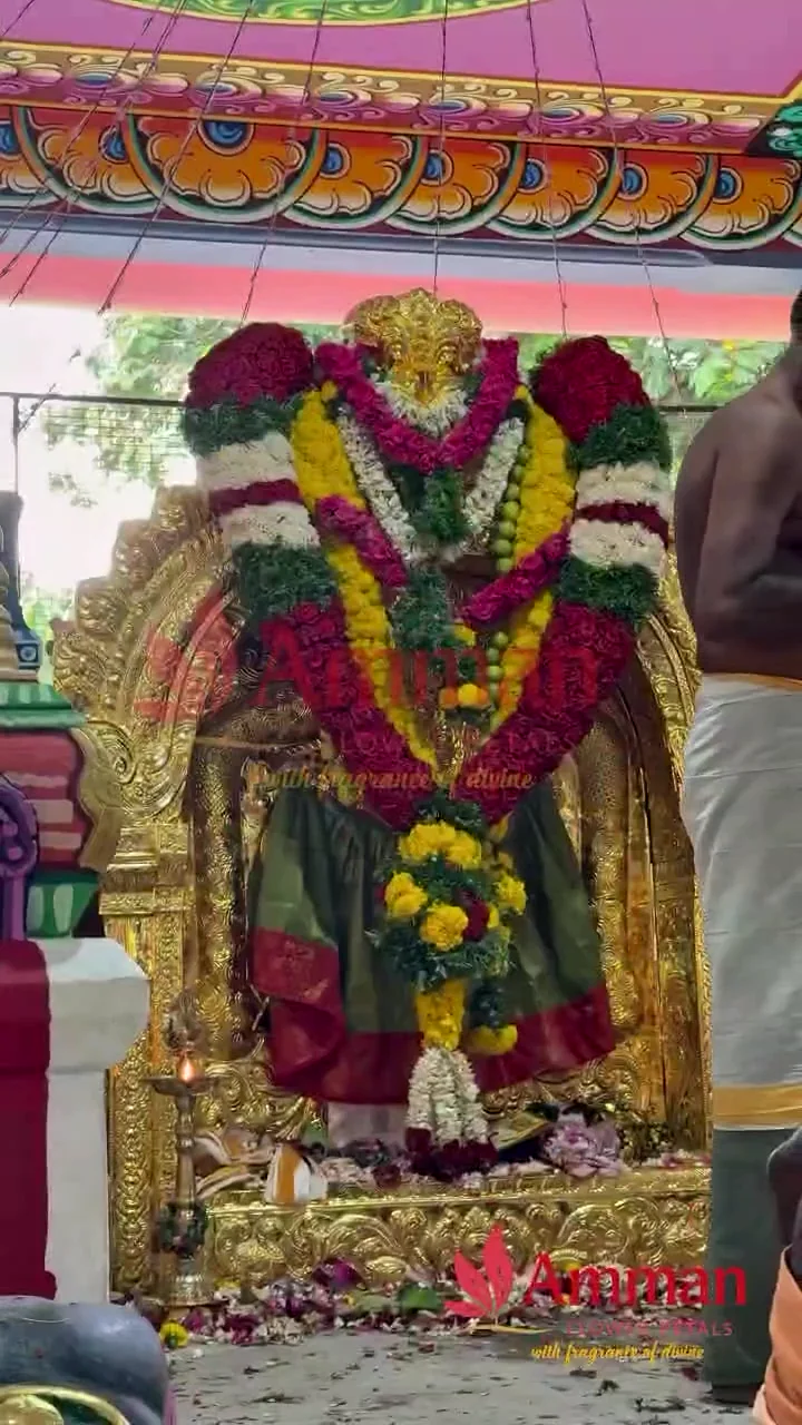 A temple deity decorated with red, yellow, white and green floral garlands
